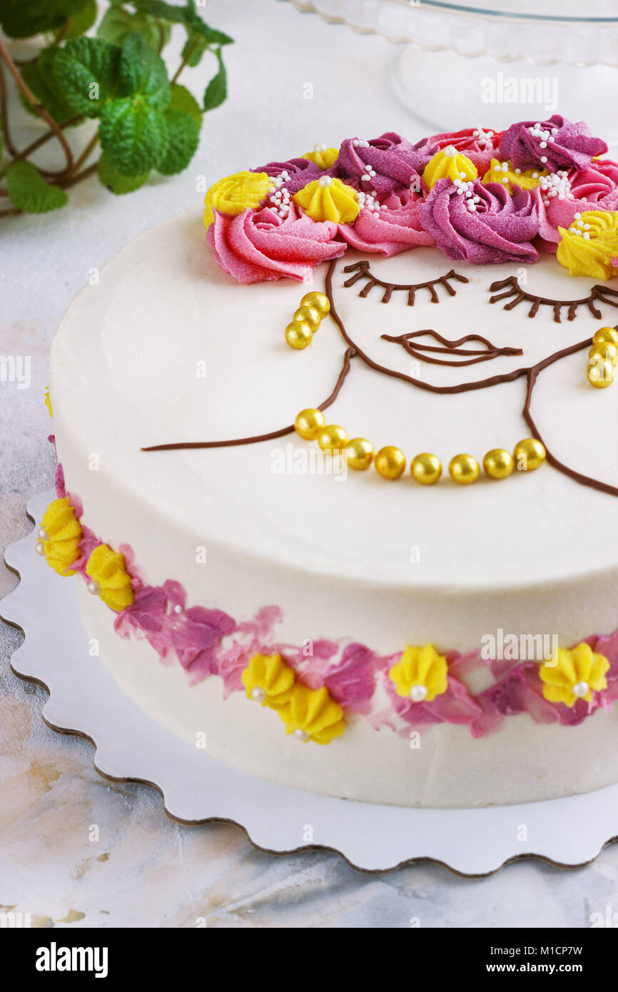 Gâteau de fête avec des fleurs crème et une fille visage sur un fond clair Banque D'Images