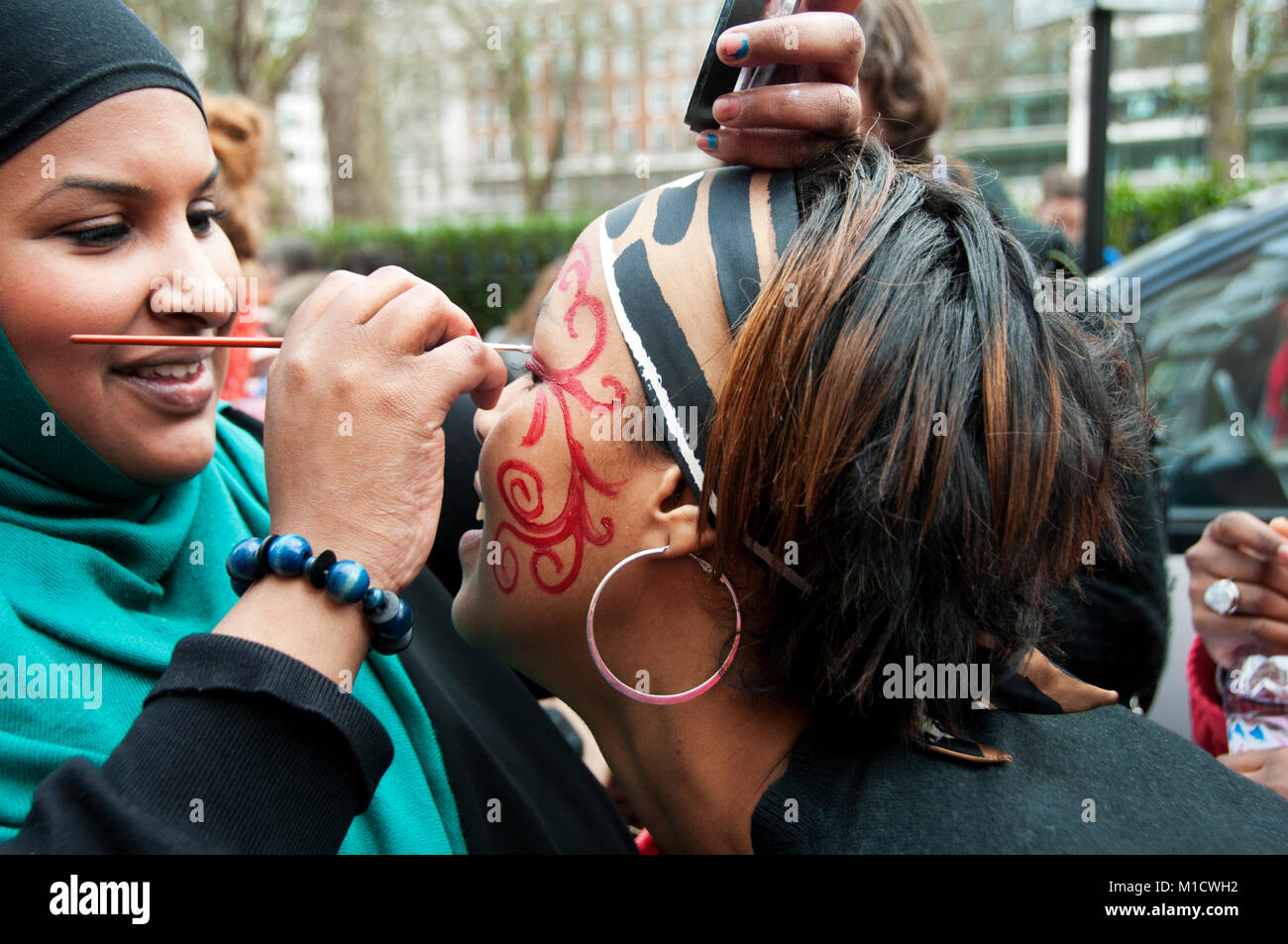 La Journée internationale de la femme le 8 mars 2009. Une femme portant un voile peint le visage d'une femme afro-antillaise Banque D'Images
