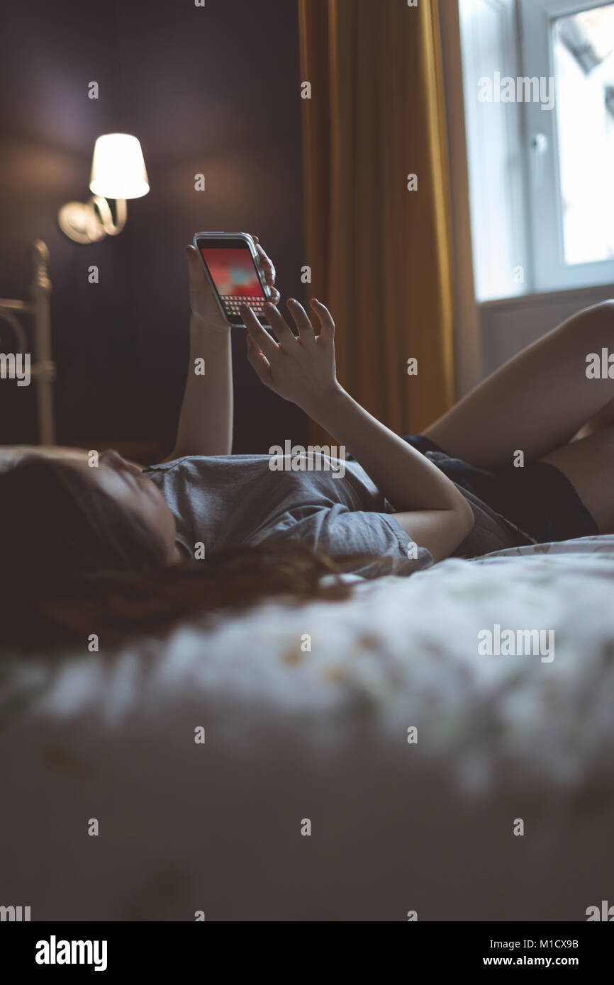 Woman using mobile phone in bedroom Banque D'Images