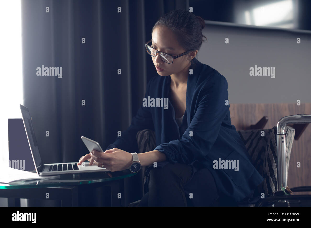 Woman using mobile phone and laptop at table Banque D'Images