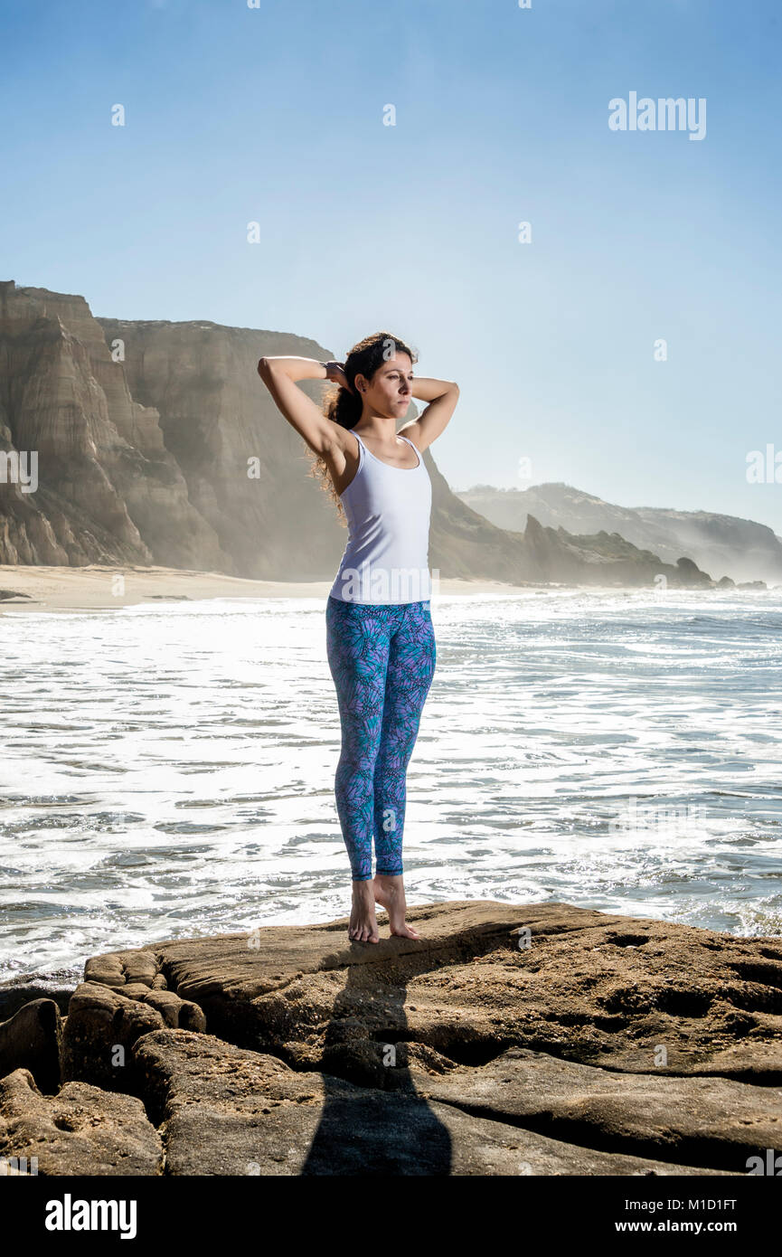 Woman practicing yoga et pilates à la plage, debout sur les rochers, les étirer sur la pointe des pieds Banque D'Images