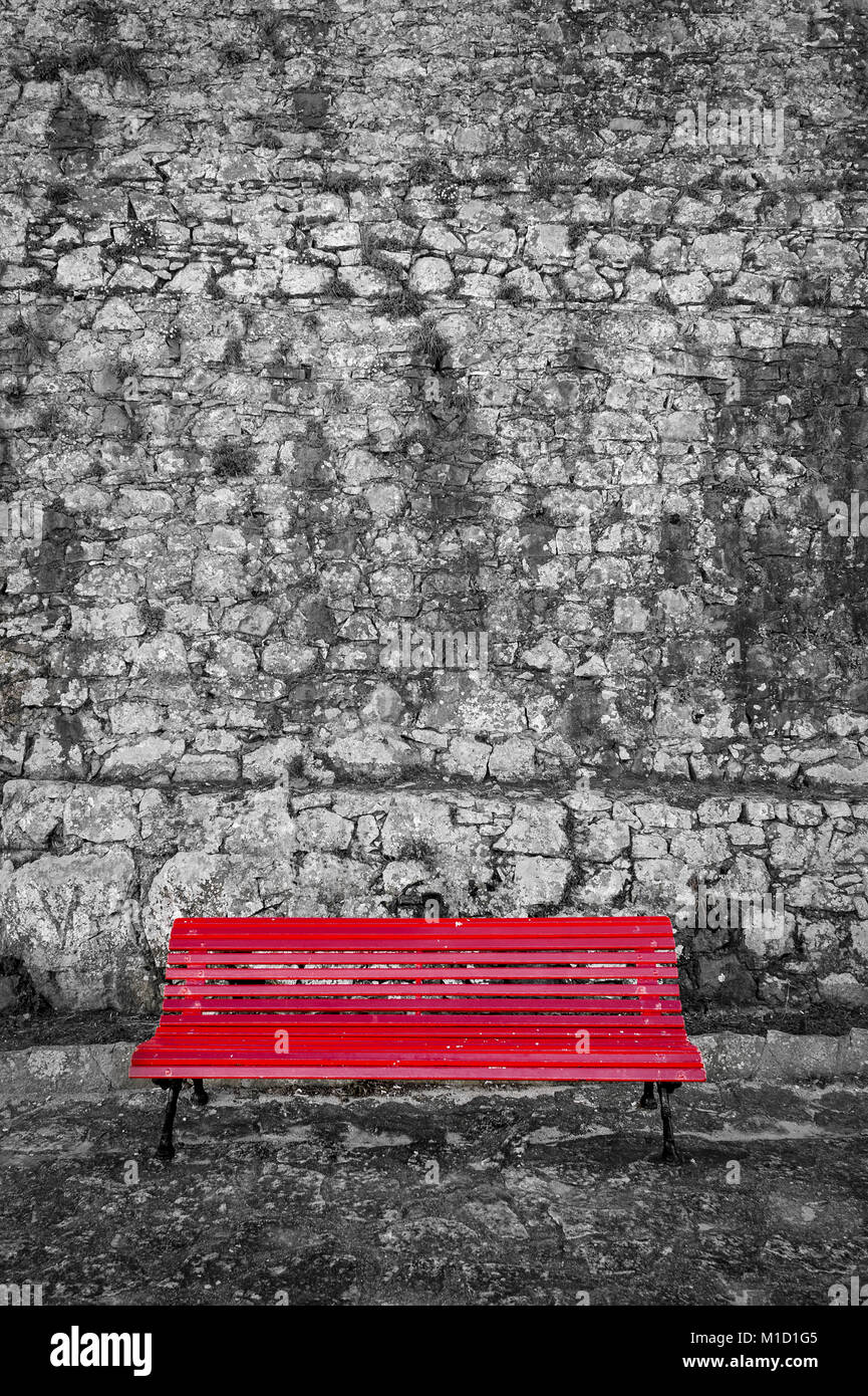 Banc peint rouge contre un vieux mur de pierre. Le noir et blanc et rouge. Banque D'Images