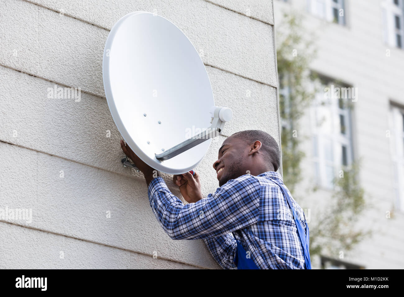 Jeune homme africain en uniforme pose plat satellite Dish On Wall Banque D'Images