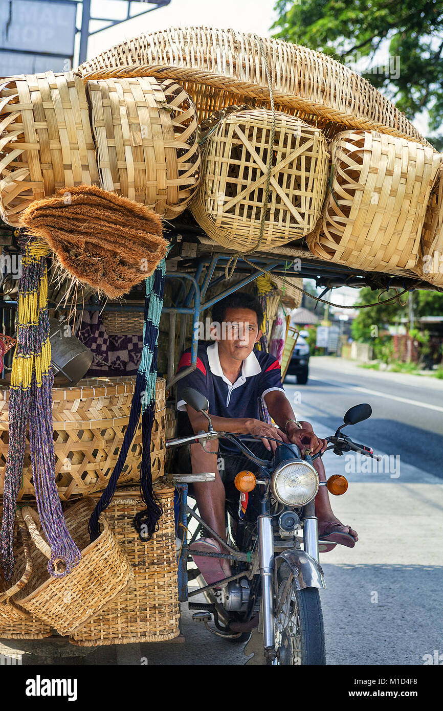 Portrait d'un vendeur qui vend des paniers en rotin et d'autres éléments de sa moto le long de la route dans la région de Luçon, aux Philippines. Banque D'Images