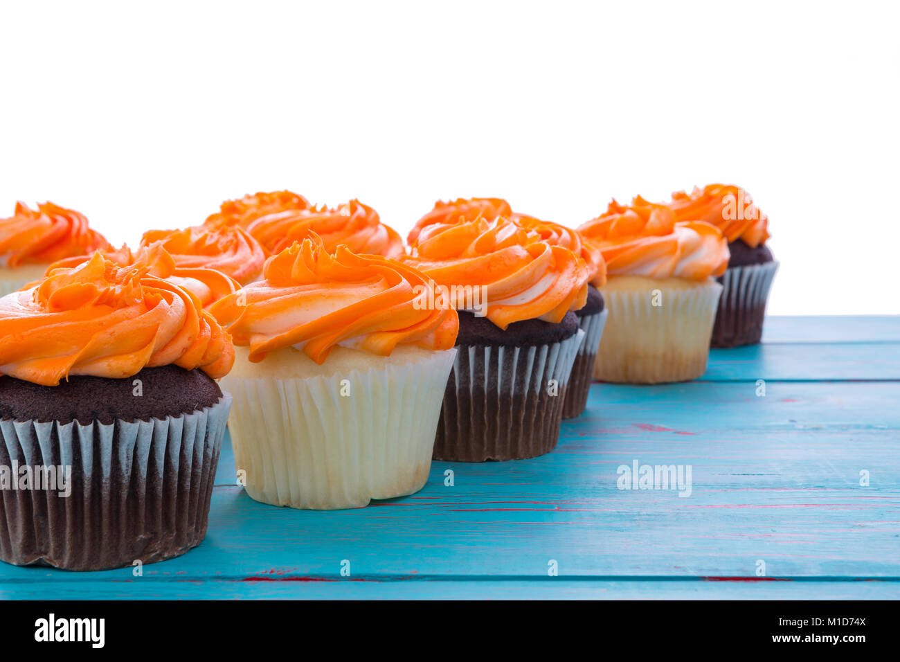 Cupcakes vanille et chocolat en alternance dans une ligne diagonale fuyante avec dégivrage et fit tourner orange colorés copy space Banque D'Images