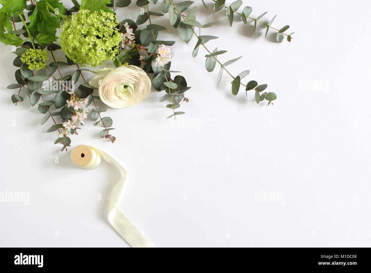 Mariage, anniversaire féminin desktop maquette des lieux. Carte de vœux papier vierge et bouquet de branches d'eucalyptus, roses et fleurs renoncule de Perse. Arrière-plan du tableau blanc. Mise à plat, vue du dessus. Banque D'Images
