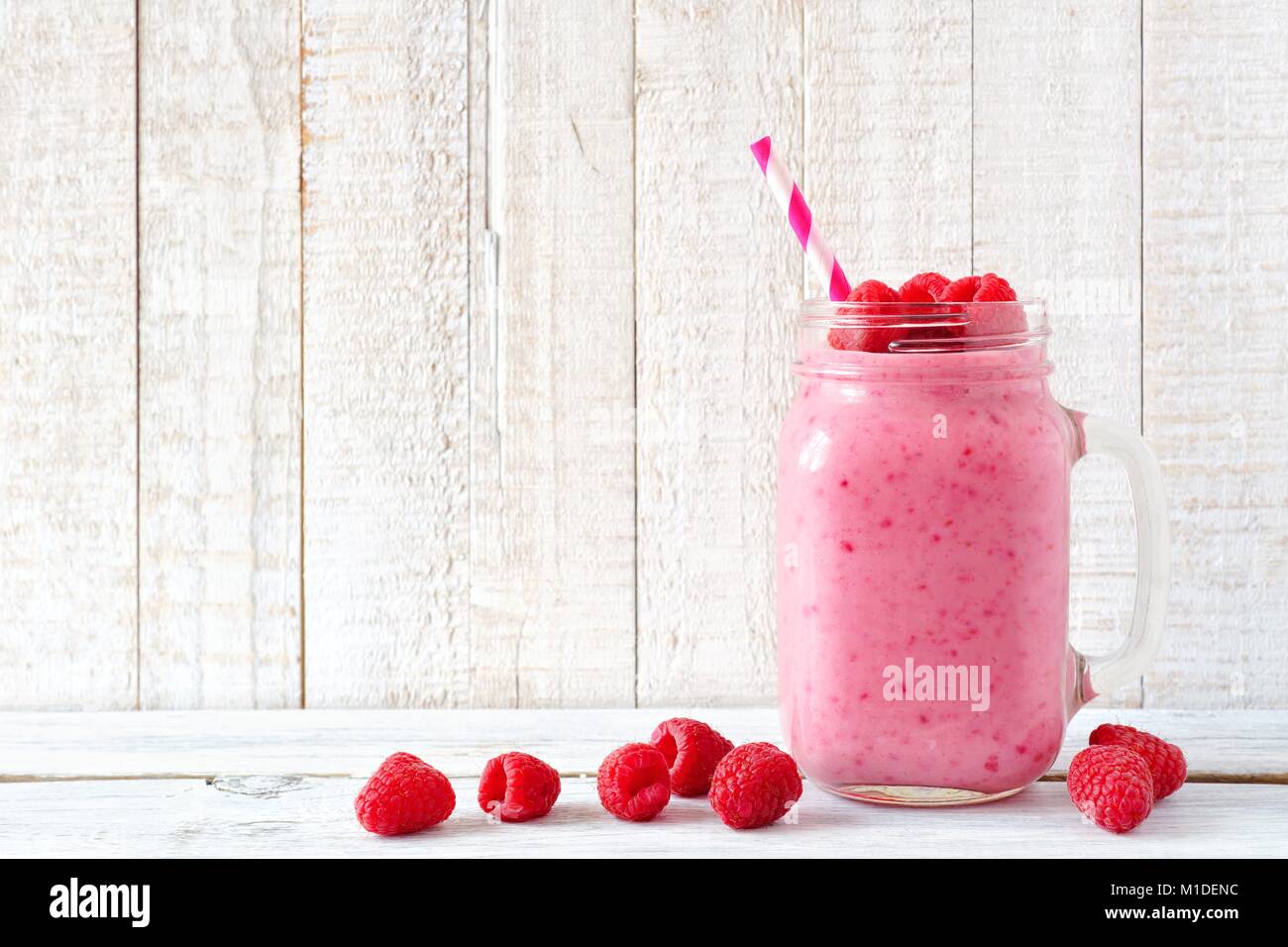 Smoothie aux framboises sain dans un pot Mason avec baies de verre éparpillés sur un fond de bois blanc Banque D'Images