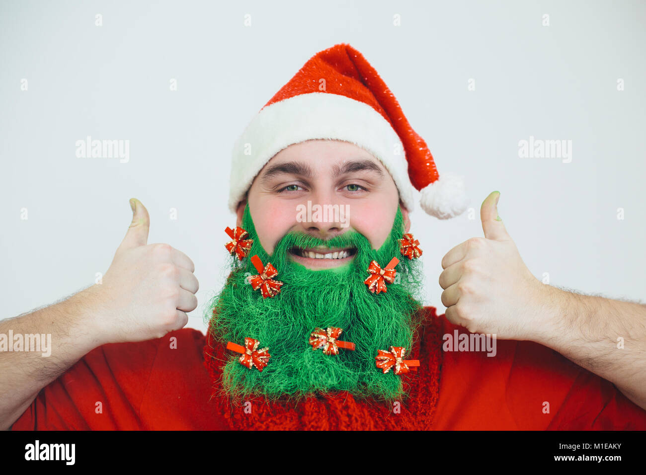 Le Père Noël en rouge vêtements avec barbe rouge vert décoré d'arcs-pouce montre des signes et sourire Banque D'Images