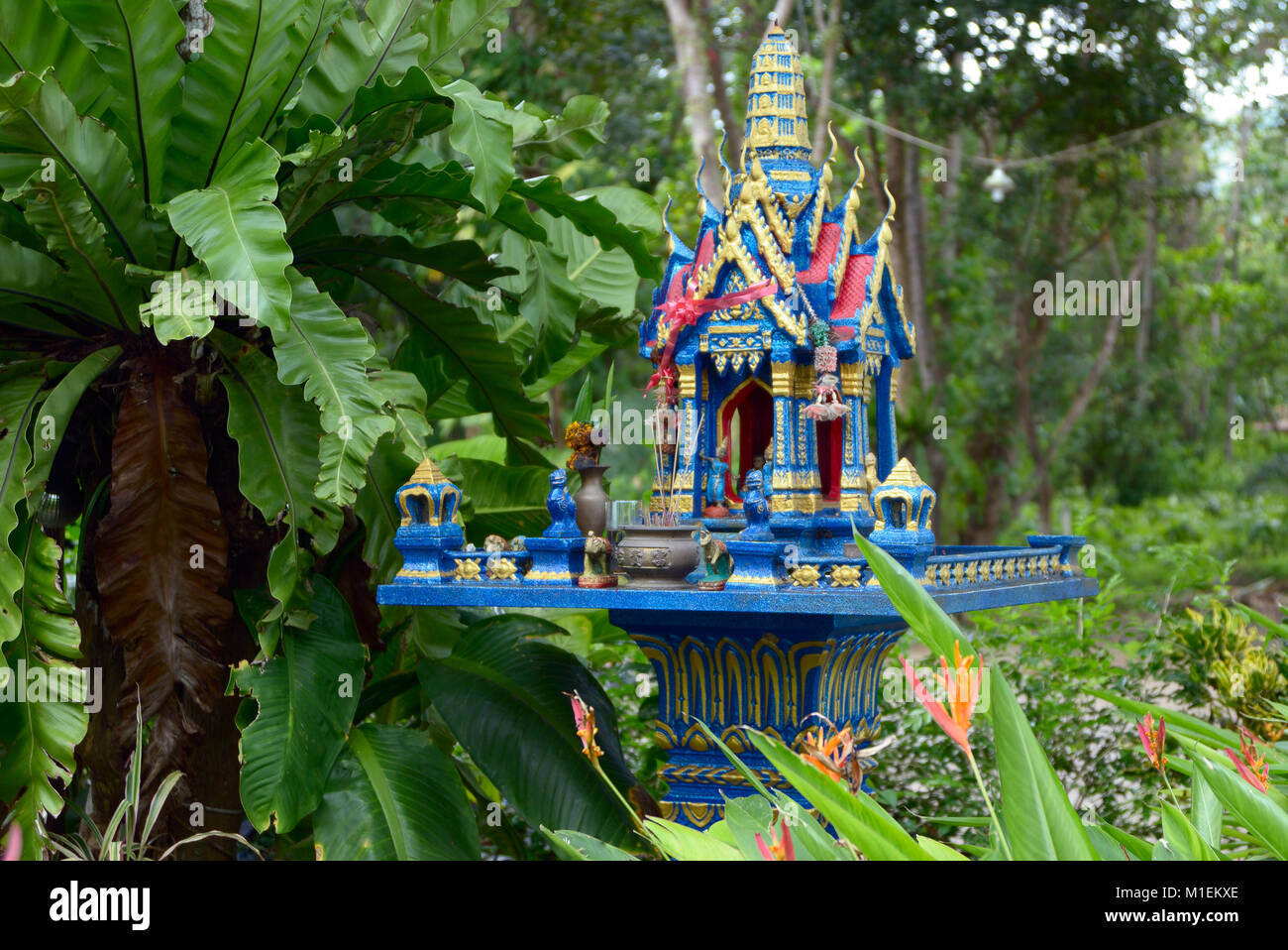 Thai spirit house avec offrande de fleurs et boissons rouge en Thaïlande. Banque D'Images