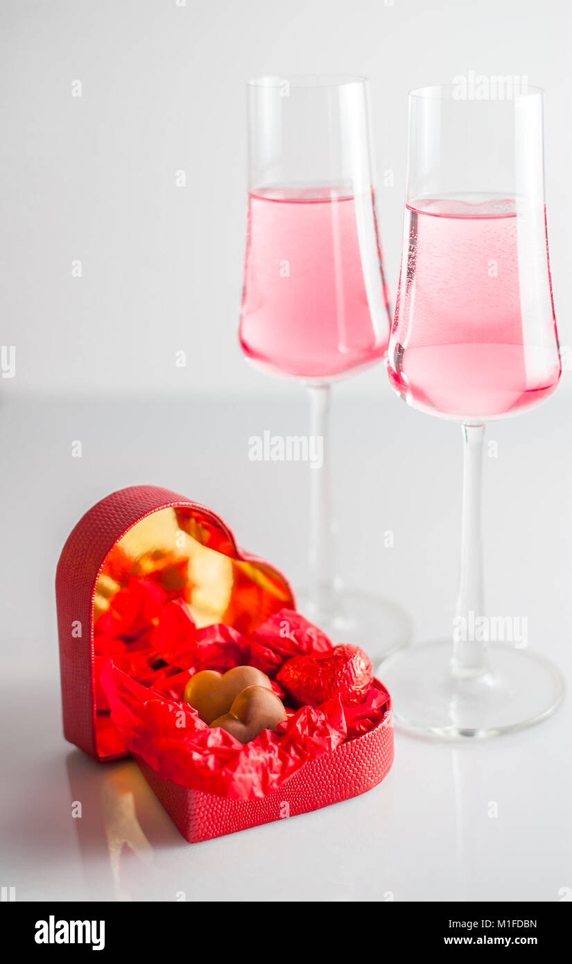 Coeurs en chocolat en forme de cœur rouge fort , et deux verres de champagne rose. fond blanc. focus sélectif. Banque D'Images