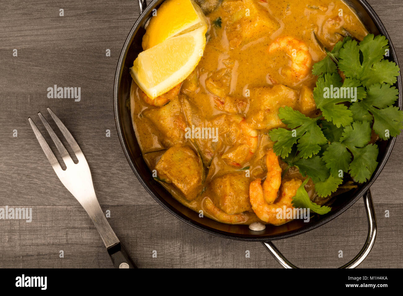 Sri Lanka King Style Gambas au curry avec du citron et de la coriandre herbes sur une table en bois foncé Banque D'Images