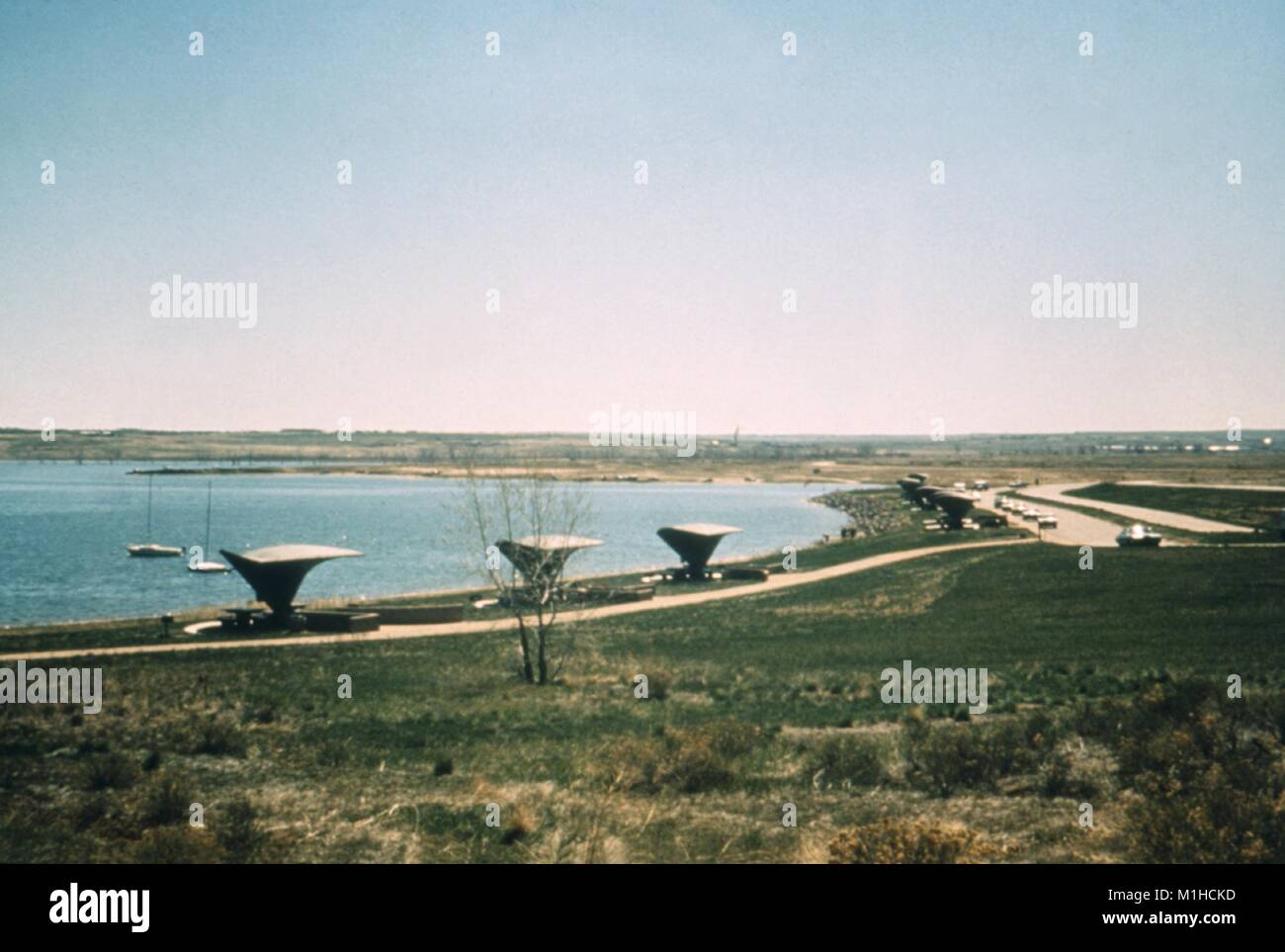 Une photographie d'un lac dans le Colorado, avec des abris de pique-nique sur la rive, l'herbe verte et de la route avec des voitures à côté, un site pertinent pour l'enquête du CDC de maladies transmises par vecteur dans et autour de l'évolution des ressources en eau, 1976. Image courtoisie CDC. () Banque D'Images Une photographie d'un lac dans le Colorado, avec des abris de pique-nique sur la rive, l'herbe verte et de la route avec des voitures à côté, un site pertinent pour l'enquête du CDC de maladies transmises par vecteur dans et autour de l'évolution des ressources en eau, 1976. Image courtoisie CDC. () Banque D'Images