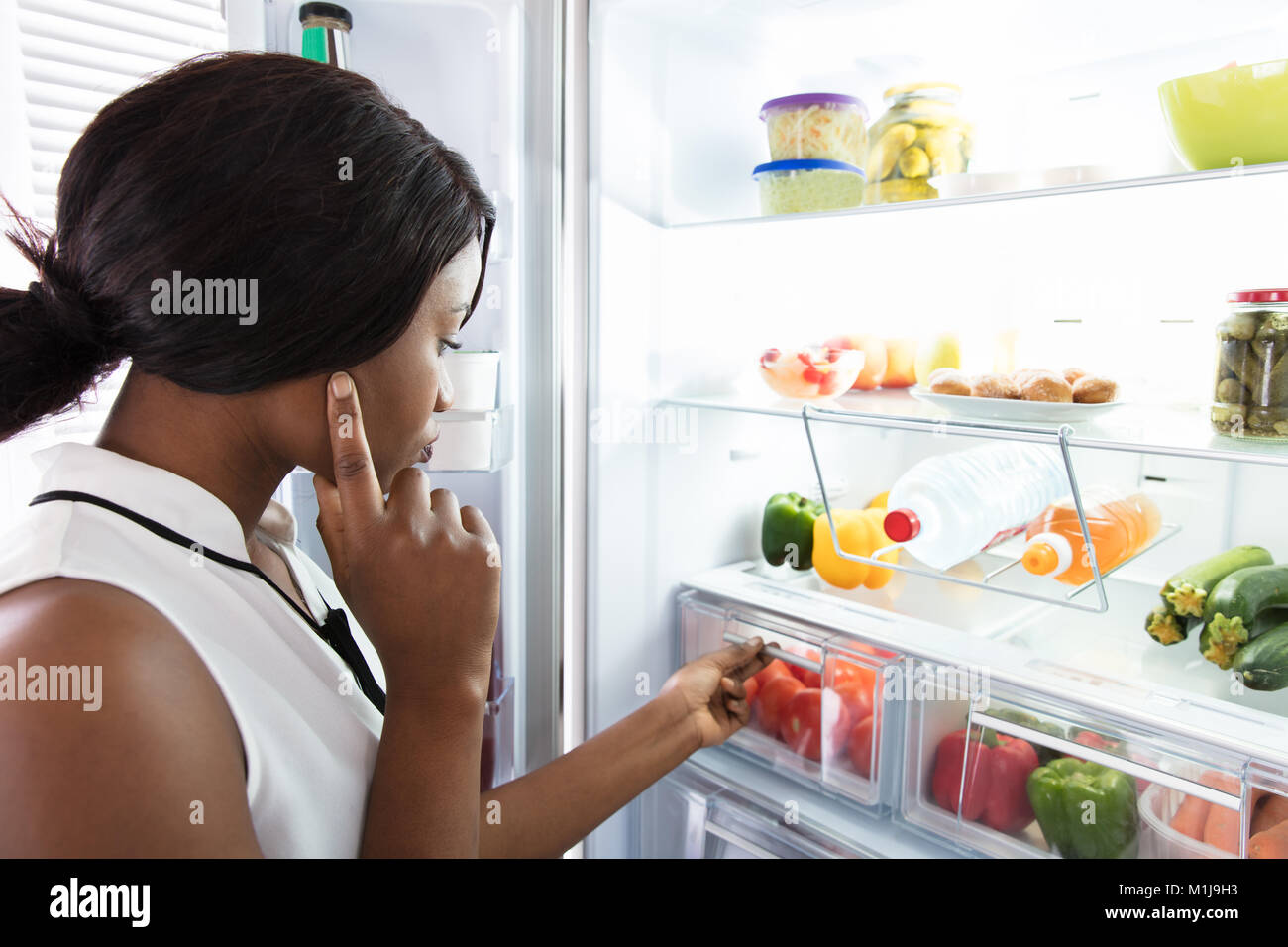 Jeune femme à la recherche d'un réfrigérateur dans la cuisine à Banque D'Images