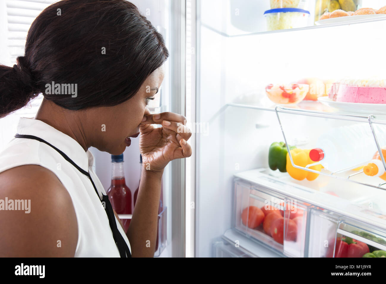 Close-up d'une jeune femme tenant son nez près de mauvais aliments dans réfrigérateur Banque D'Images