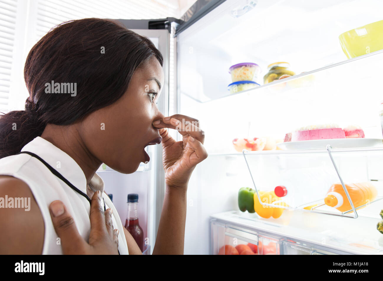 Close-up d'une jeune femme tenant son nez près de mauvais aliments dans réfrigérateur Banque D'Images