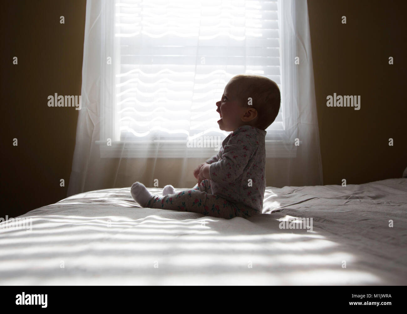 Profil de Laughing Baby Sitting on Bed Banque D'Images