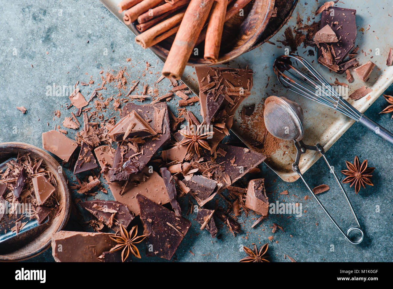 Brisures de chocolat noir, cannelle et anis étoile sur un fond en béton avec une crépine de cacao et d'un fouet avec vitrage. Photographie alimentaire confiserie Banque D'Images