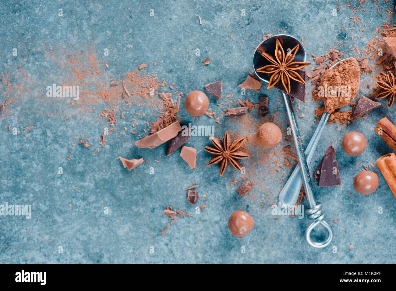 Mise à plat avec des cuillères, des pièces en chocolat, d'épices, d'anis étoile, la cannelle et cacao sur un fond de pierre. Ingrédients pour un dessert. Douceurs maison phot Banque D'Images