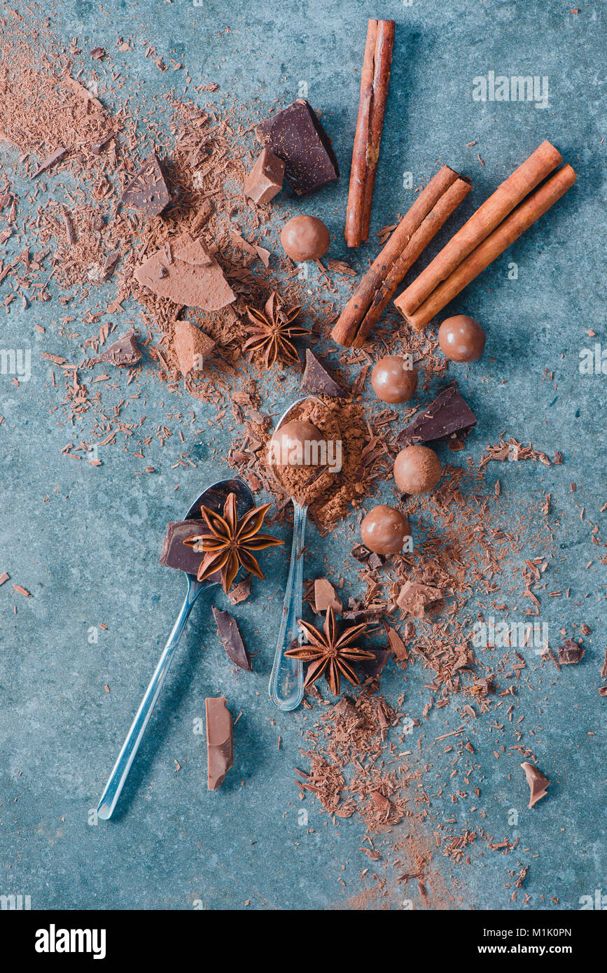 Mise à plat avec des cuillères, des pièces en chocolat, d'épices, d'anis étoile, la cannelle et cacao sur un fond de pierre. Ingrédients pour un dessert. Douceurs maison phot Banque D'Images