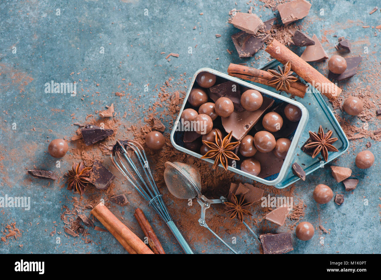 Des chocolats faits maison et des morceaux de chocolat cassé avec des épices, l'anis étoile, la cannelle et cacao sur un arrière-plan en pierre rustique dans une boîte en métal. Confectio Banque D'Images