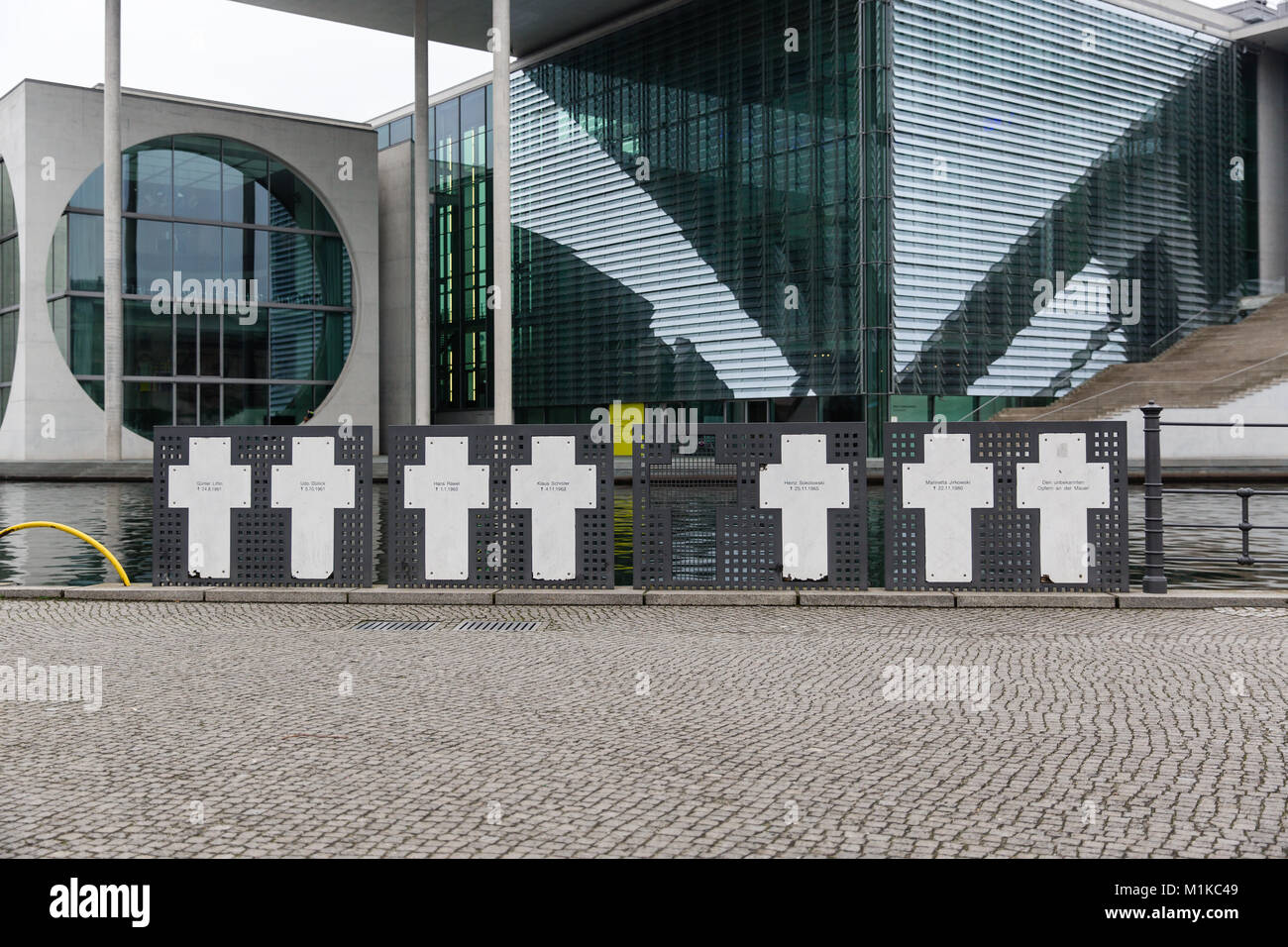 La croix commémorant les victimes du Mur de Berlin à la Spree avec à côté des bâtiments modernes de gouvernement allemand dans l'arrière-plan. Banque D'Images