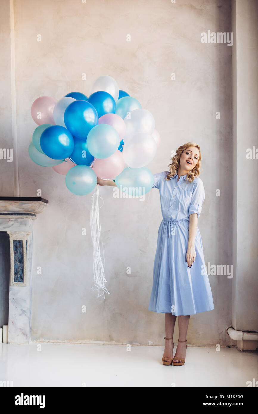 Femme blonde en robe bleu clair bleu et rose baloons rester en face d'un mur de lumière Banque D'Images