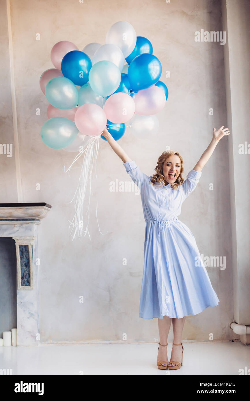 Femme blonde en robe bleu clair bleu et rose baloons rester en face d'un mur de lumière Banque D'Images