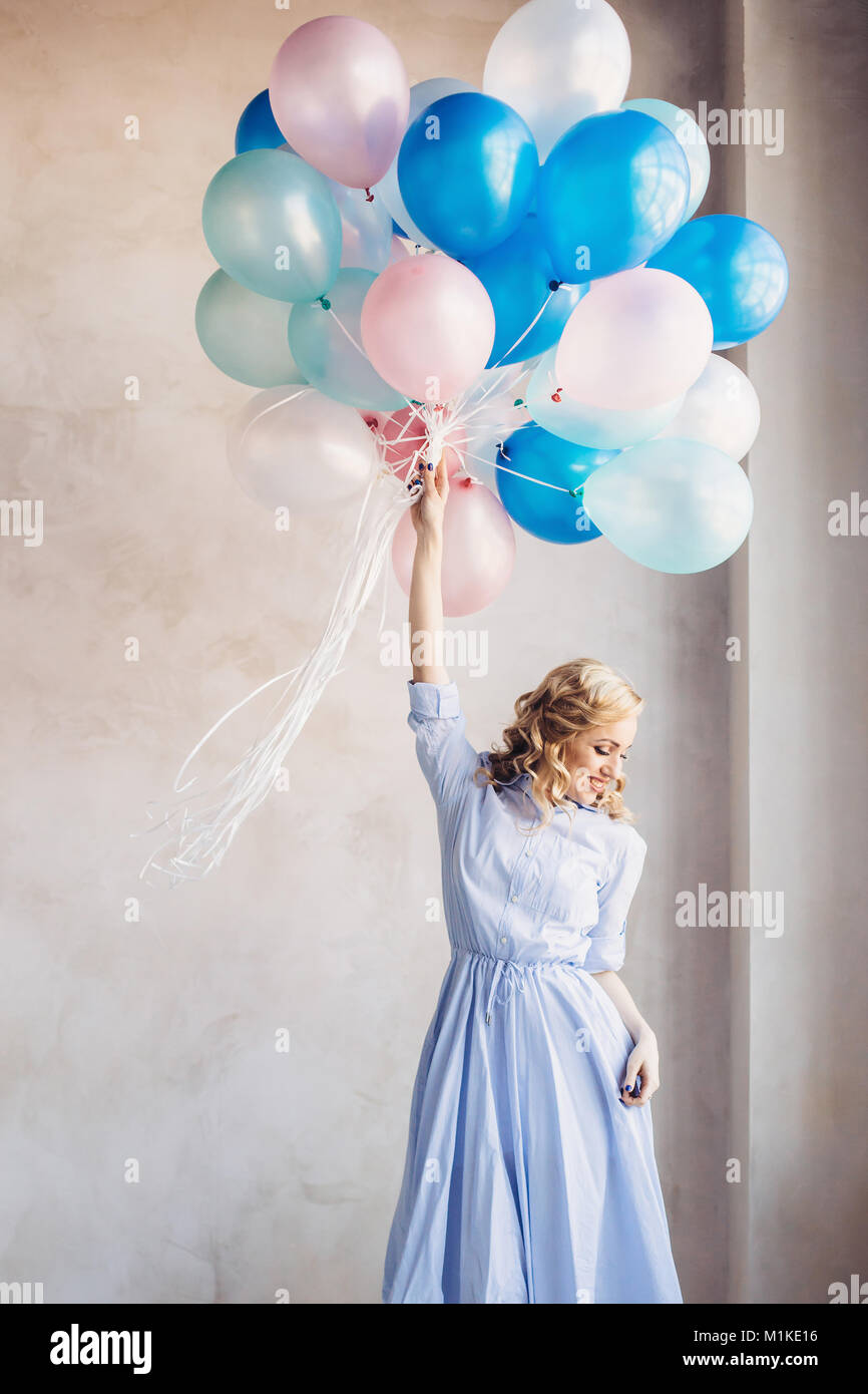 Femme blonde en robe bleu clair bleu et rose baloons rester en face d'un mur de lumière Banque D'Images