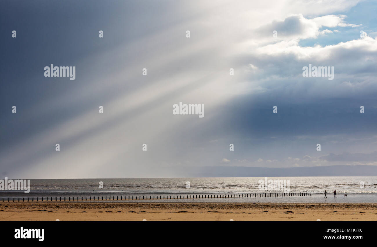 Un homme et femme marche un chien sur la plage à l'Est Brean côte du Somerset comme une douche lourde de pluie s'efface pour révéler le ciel bleu et le soleil Banque D'Images
