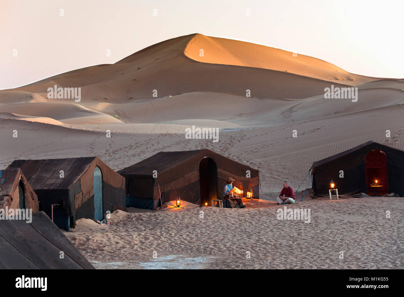 Le Maroc, Mhamid, Erg Chigaga dunes de sable. Désert du Sahara. Camp de vacances, un bivouac. Les touristes, en couple, en face de la tente au coucher du soleil. Banque D'Images