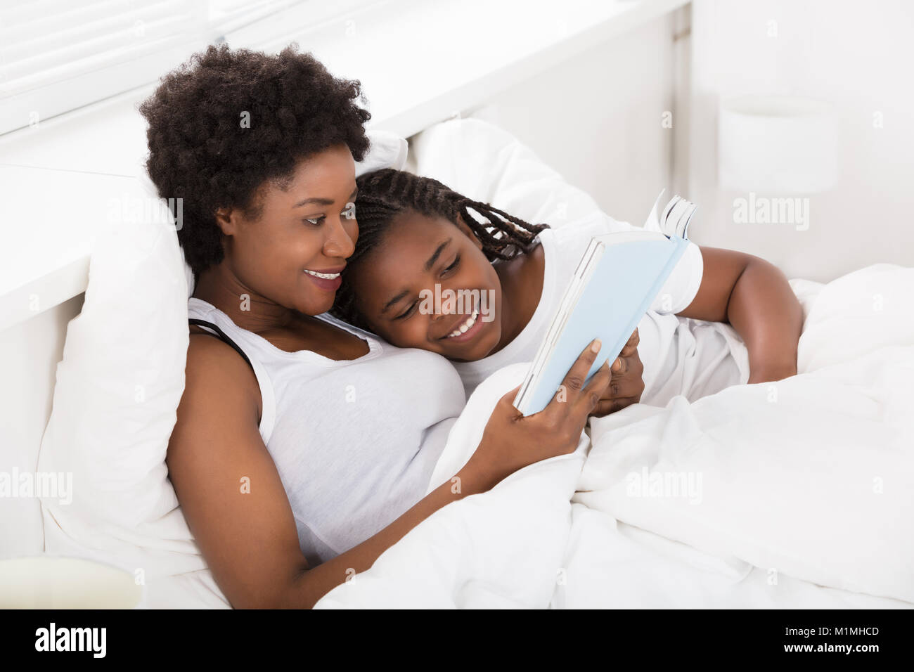 Lecture de la mère une Histoire Livre à sa fille au lit Banque D'Images