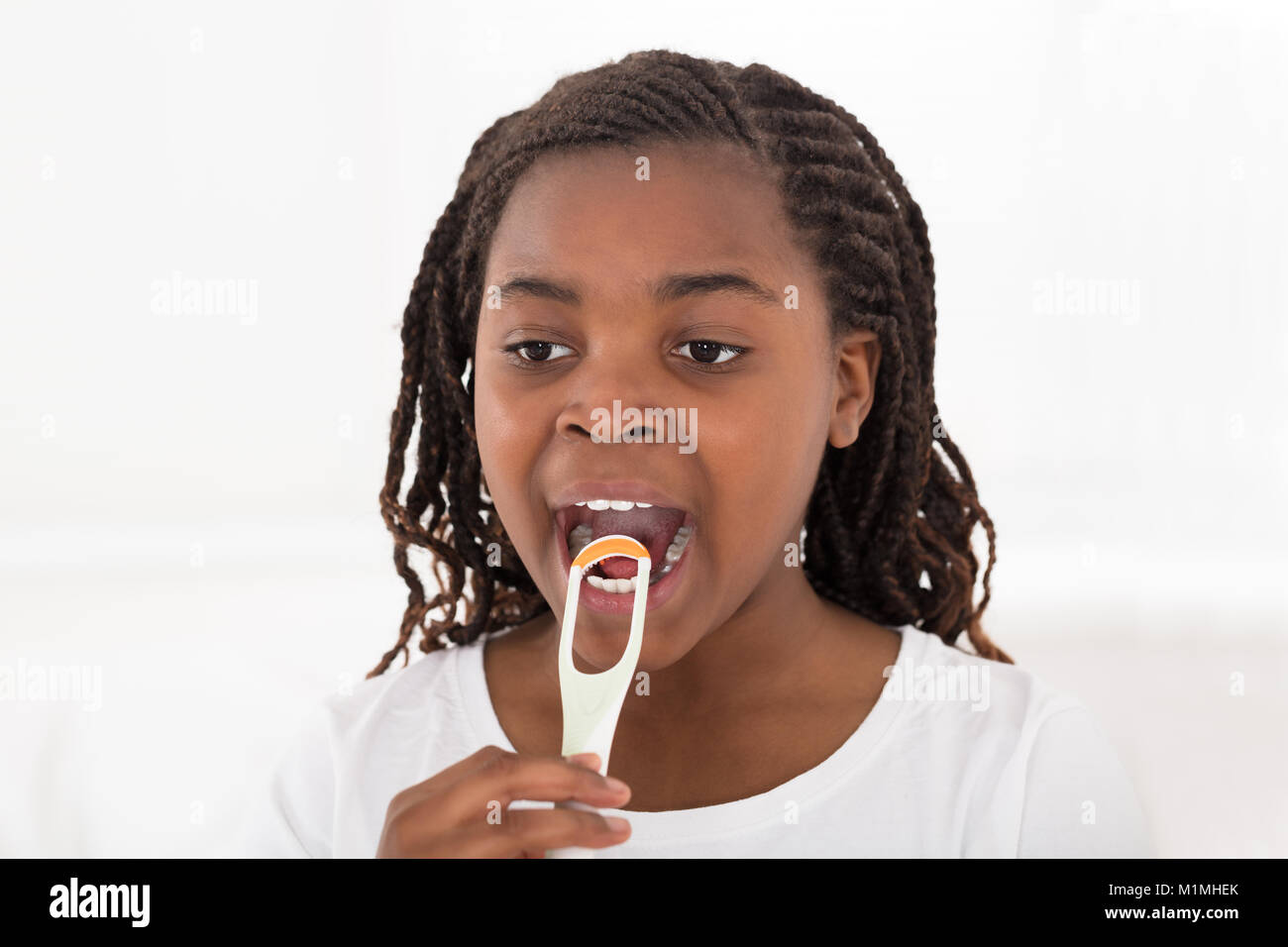 Portrait d'une jeune fille africaine sa langue de nettoyage avec grattoir sur fond blanc Banque D'Images