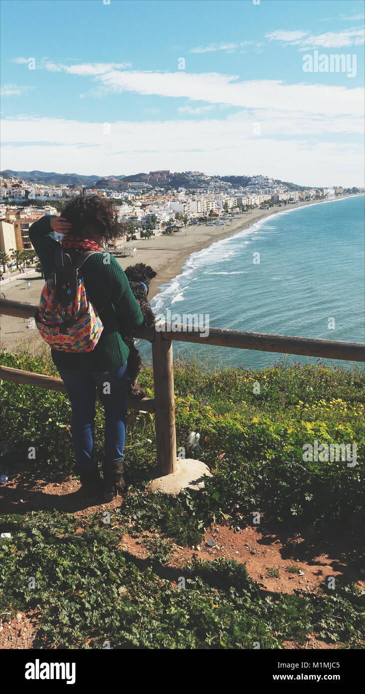 Femme tenant son chien contre les rampes regardant la vue sur la plage, Malaga, Andalousie, Espagne Banque D'Images
