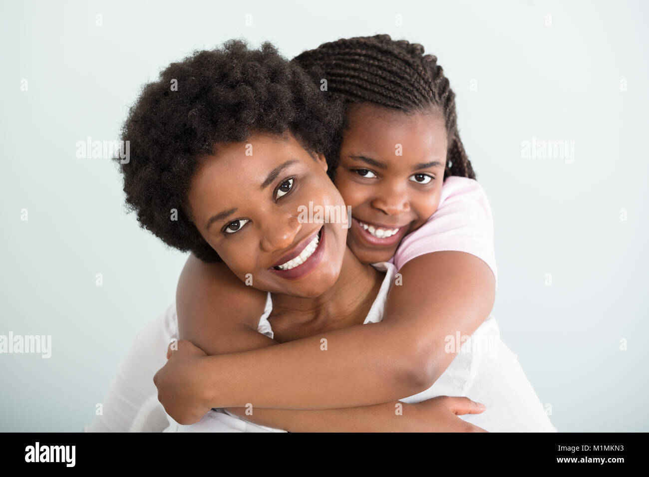 Portrait d'une fille embrassant sa mère par derrière contre fond blanc Banque D'Images