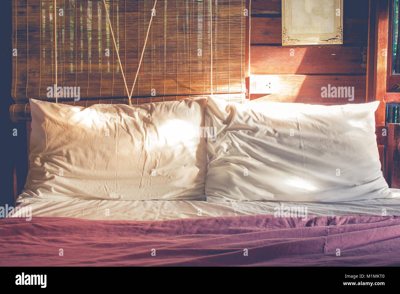 Près de deux sur l'oreiller froissé blanc lit avec soleil rayonné de droite de la chambre en matinée à temps dans la campagne de style vintage. Banque D'Images