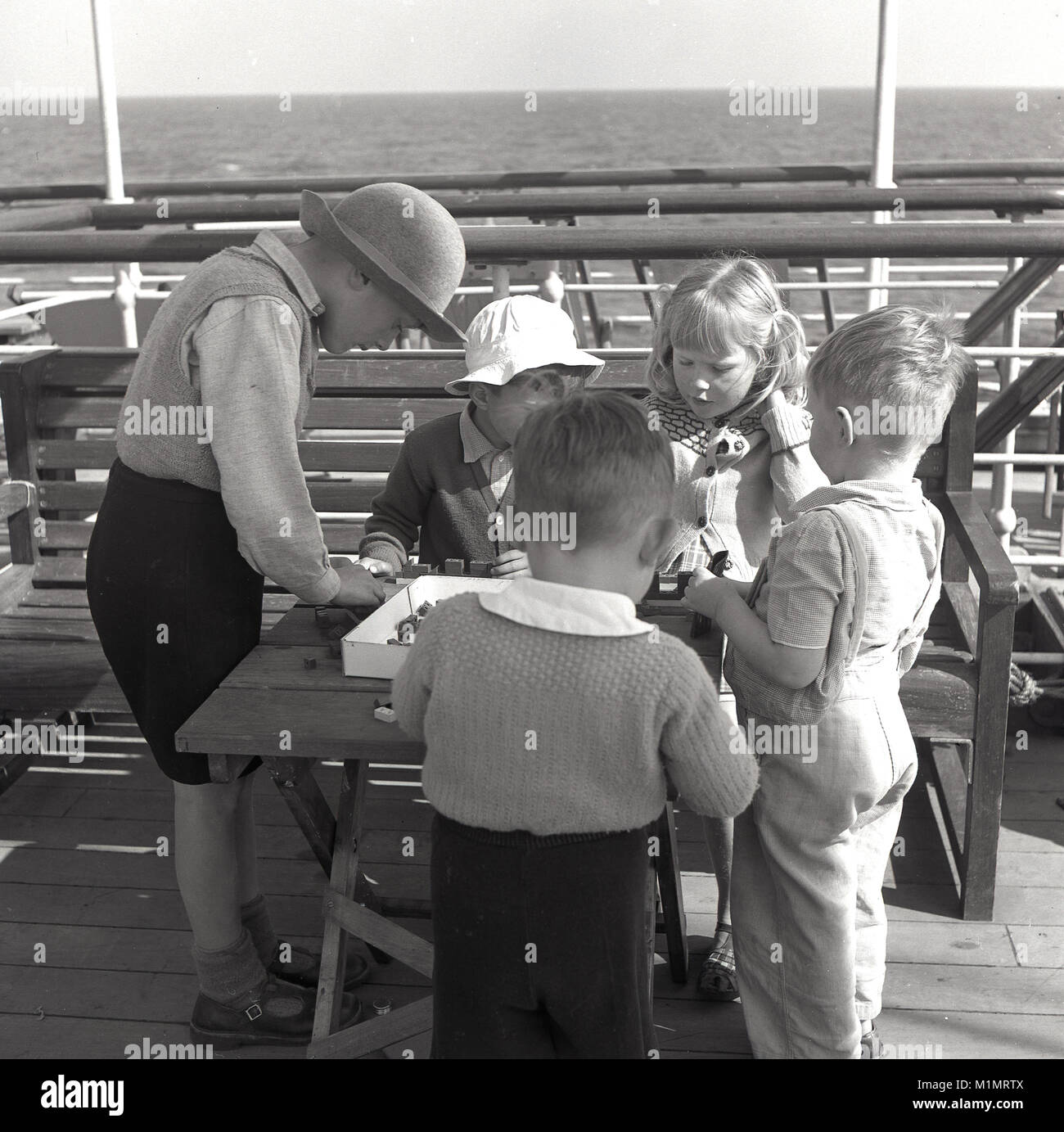 Années 1950, historique, sur l'océan à bord d'un bateau à vapeur Union-Castle dirigé pour une nouvelle vie en Afrique du Sud, un groupe de jeunes enfants jouer avec les petits jouets en plastique sur la construciton d'une petite table à l'extérieur sur le pont du navire. Banque D'Images