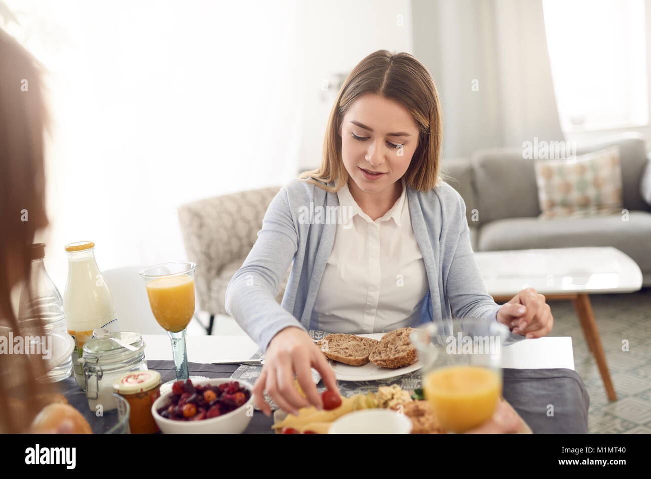 Jolie jeune femme sourire adolescent assis à une table avec sa meilleure amie prendre le petit-déjeuner et en tournant et en tenant une tomate fraîche Banque D'Images
