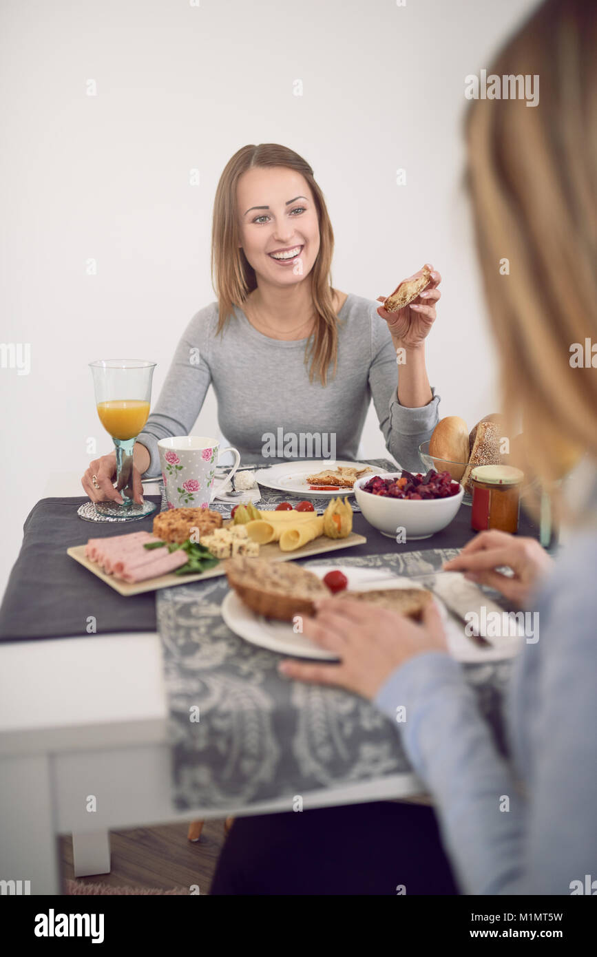Jolie jeune femme d'adolescent avec un sourire plein de vivacité assis à une table avec sa meilleure amie prendre le petit-déjeuner et en tournant pour sourire à l'appareil photo Banque D'Images