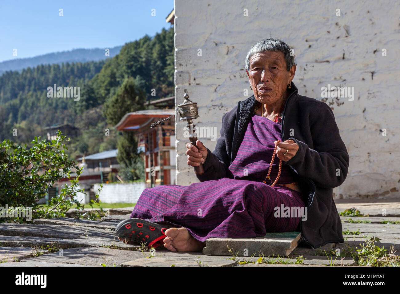 Bumthang, Bhoutan. Vieille Femme avec son moulin à prières et Chapelet, Kurje Lhakhang temple bouddhiste et son monastère. Banque D'Images