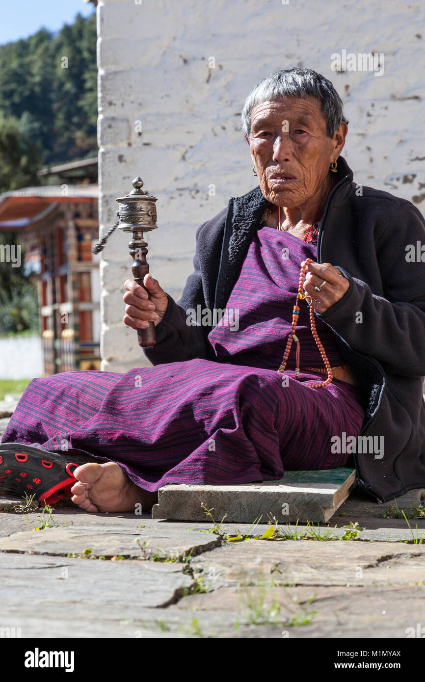 Bumthang, Bhoutan. Vieille Femme avec son moulin à prières et Chapelet, Kurje Lhakhang temple bouddhiste et son monastère. Banque D'Images