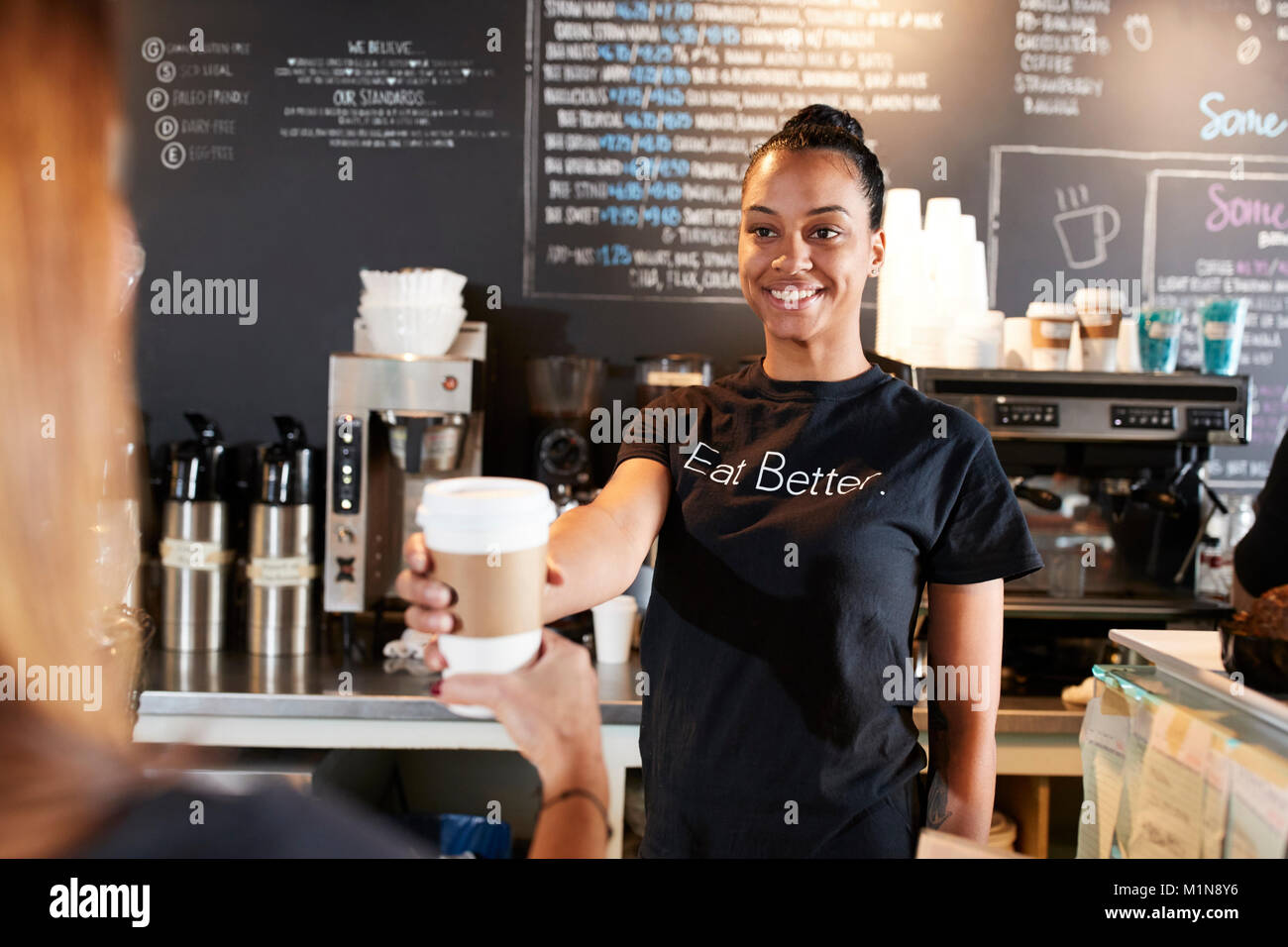 Barista femelle servant café à emporter avec client In Cafe Banque D'Images