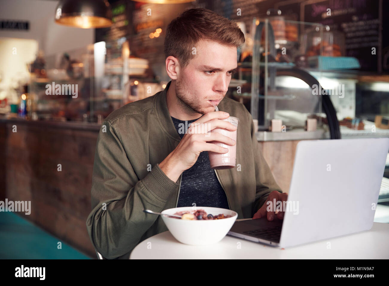 Young Man Using Laptop In Cafe tout en prenant un petit déjeuner Banque D'Images