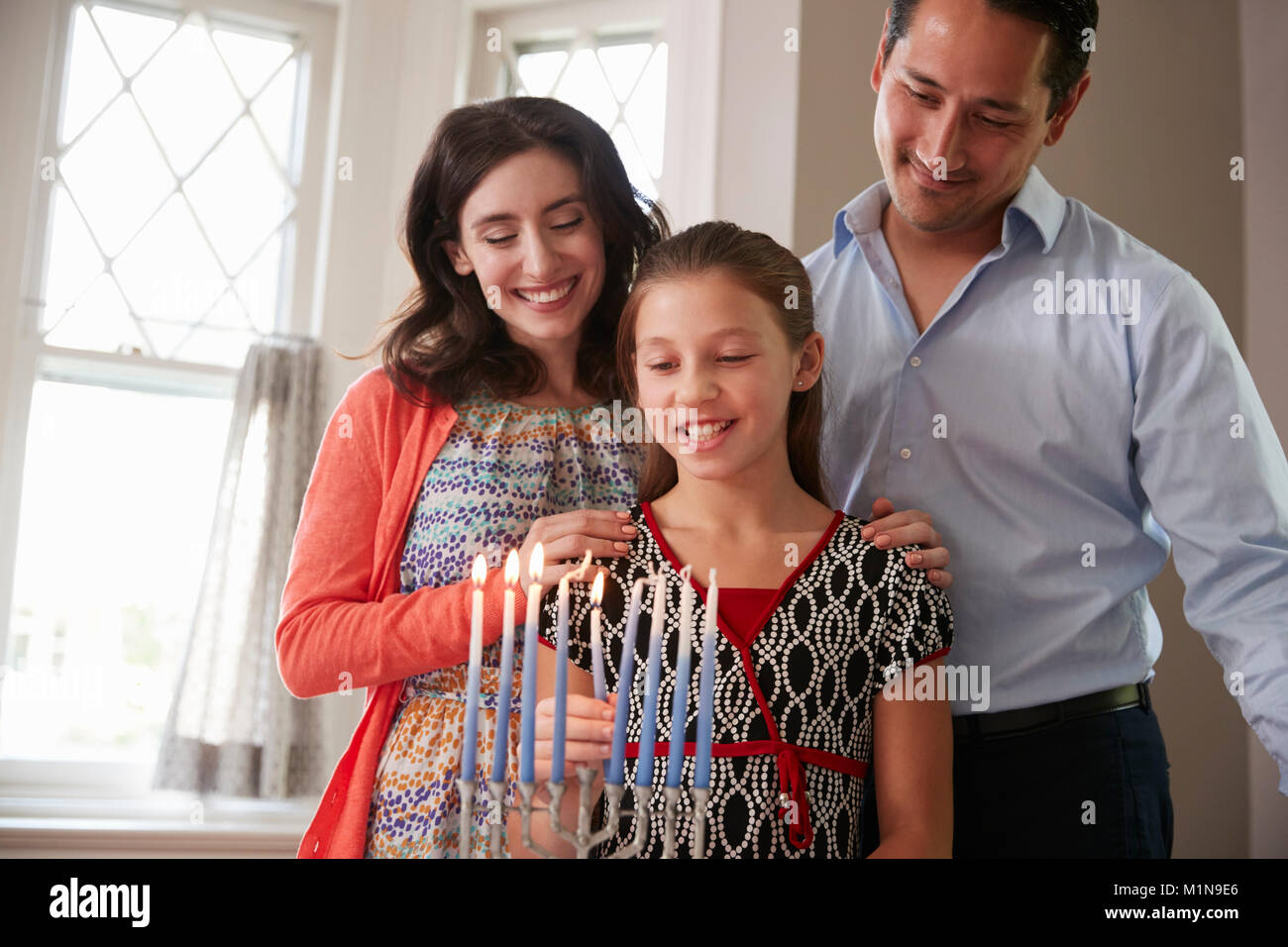 Fille de parents regarder la lumière des bougies sur la menorah pour Shabbat Banque D'Images