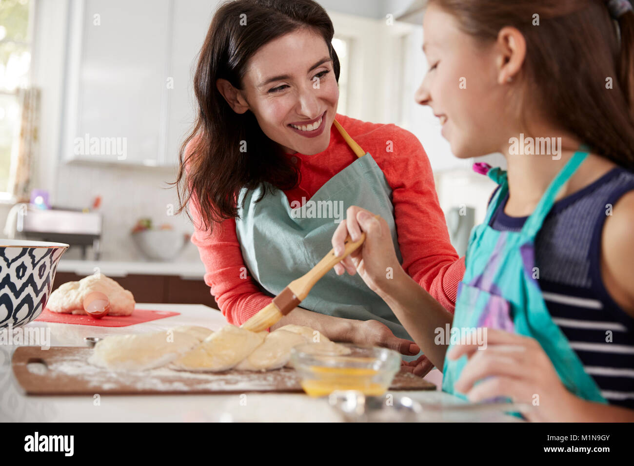Girl brushing glaze sur pâte à pain challah avec sa maman Banque D'Images
