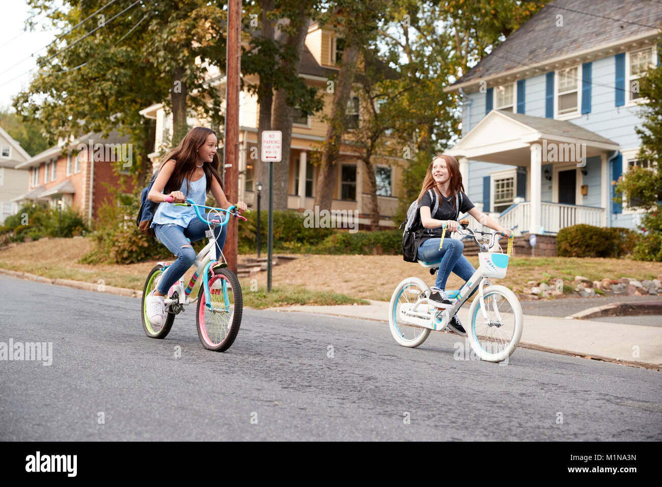 Deux copines adolescentes ride passé sur des vélos dans une rue calme Banque D'Images