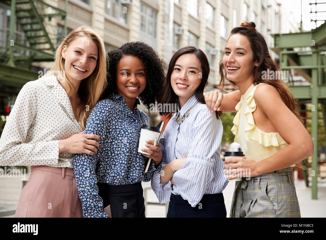Quatre collègues de sexe féminin à l'extérieur de l'appareil photo en souriant Banque D'Images