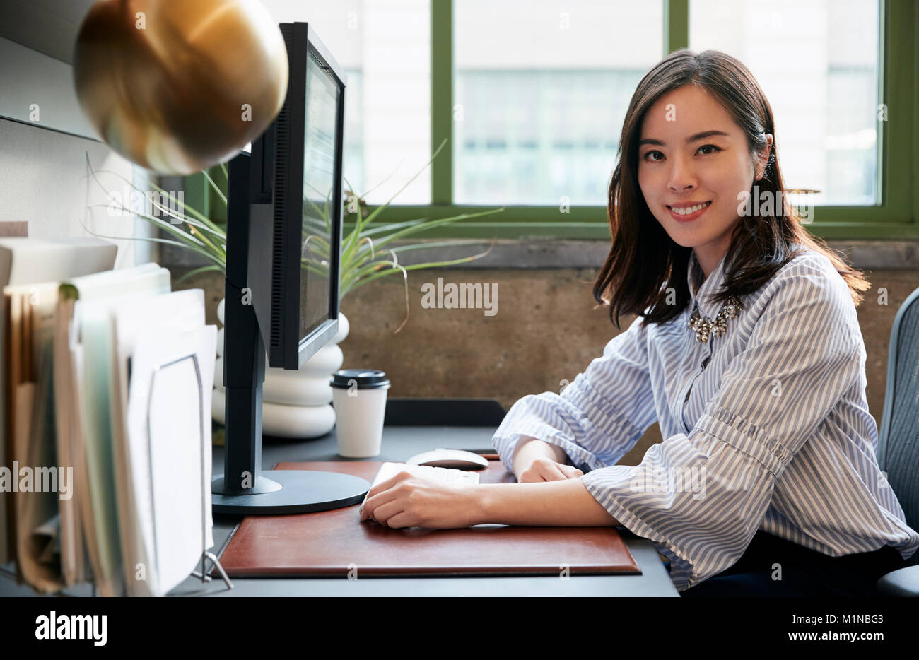 Femme chinoise à un ordinateur dans un bureau souriant pour appareil photo Banque D'Images