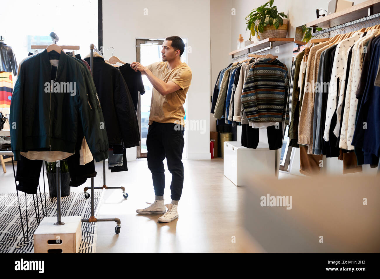 Young Hispanic man looking at clothes sur un rail dans un magasin Banque D'Images