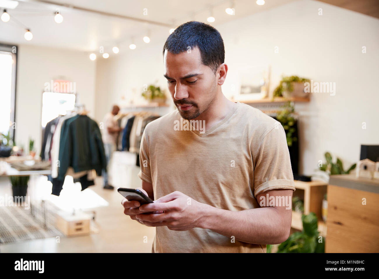 Young Hispanic man using smartphone dans un magasin de vêtements Banque D'Images