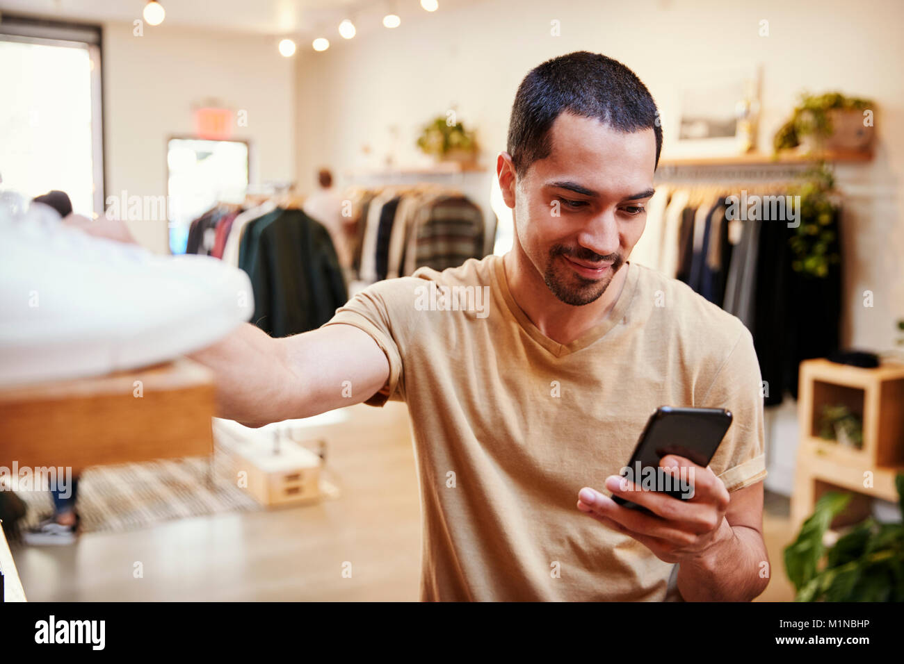 Smiling Hispanic man using smartphone dans un magasin de vêtements Banque D'Images